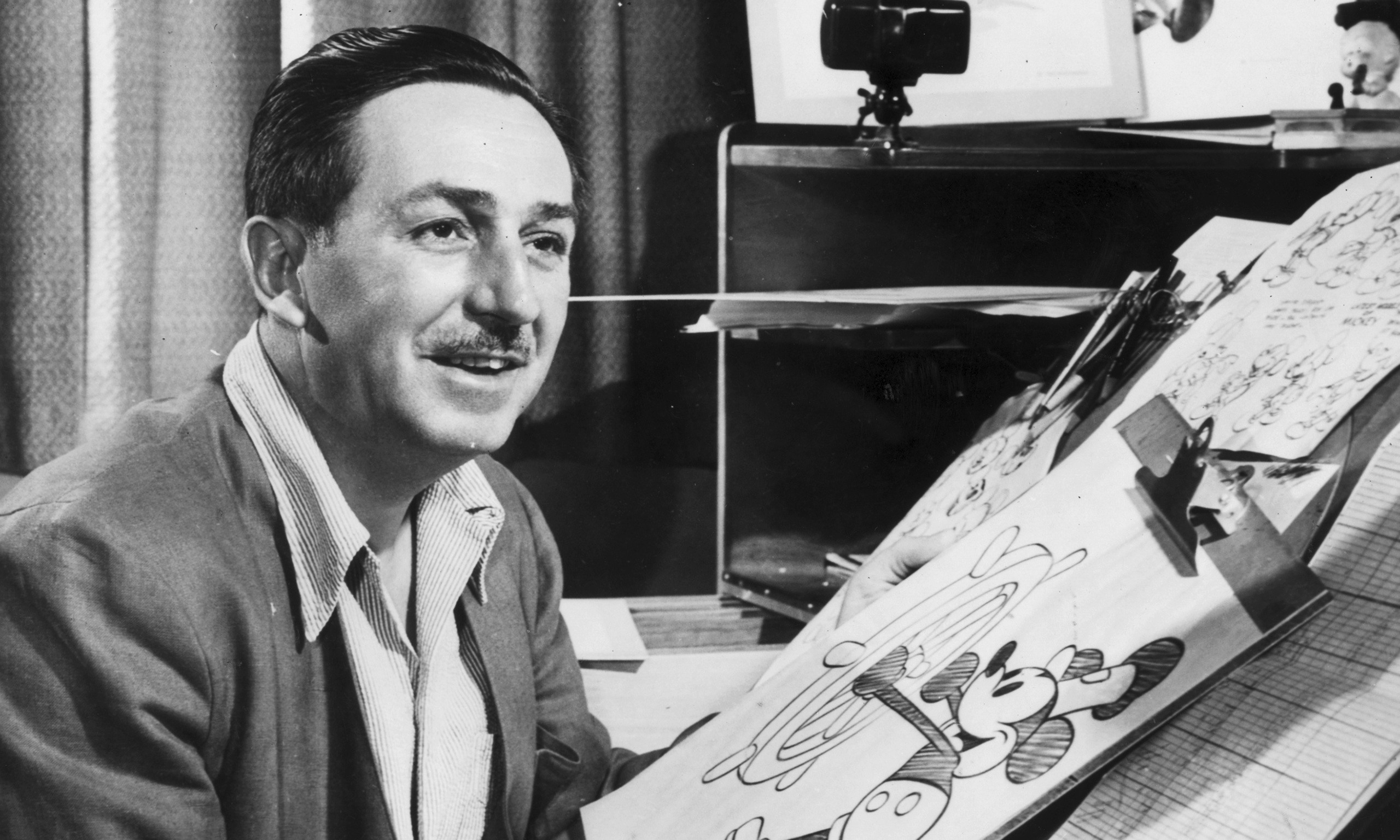 Mr Walt Disney sits at his drawing board in his studio, drawing a sketch of Mickey Mouse